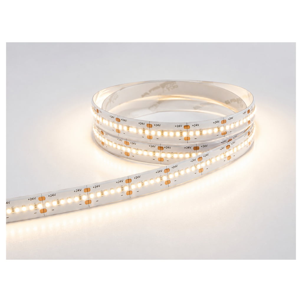 Flexible white LED strip light laid out on a white surface, showing its +24V markings and copper pads with a warm glow.
