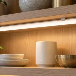 A closed tubular light retained beneath a shelf in a finished display cabinet